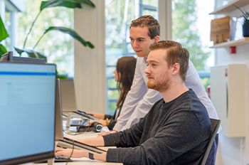 Twee medewerkers bespreken gegevens op een computerscherm in een kantooromgeving, gericht op het implementeren van het Digitaal Product Paspoort.